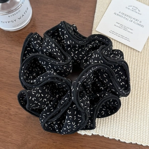 Détail d'un chouchou noir à motifs blancs sur bois et texture beige raffinée