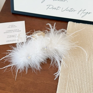 Detailed shot of white ostrich feather hair claw clip with crystals on gold alloy base