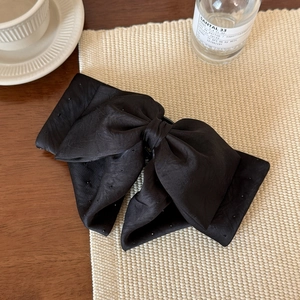 Detailed close-up of a luxury black satin bow hair clip with shimmering black rhinestones