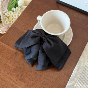 Elegant black satin bow hair claw clip with subtle starry texture on a rustic wooden table