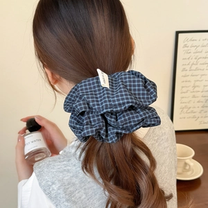 Detailansicht eines blau-karierten Haargummis mit Etikett im Haar des Models