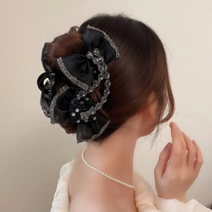 Pince à cheveux élégante avec nœud noir et strass portée sur les cheveux du modèle