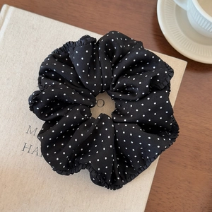 Detailed view of black and white polka dot scrunchie with ruffled edges on a book