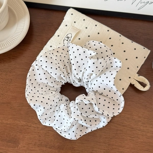 Polka dot fabric scrunchie with matching storage pouch on a minimalist wooden table