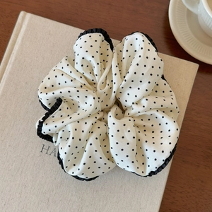 Macro detail of large white scrunchie with black polka dots and delicate ruffled edges