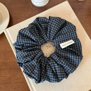 Detailansicht eines blau-schwarz karierten Haargummis mit Made in Korea-Etikett