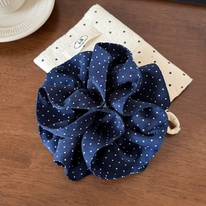 Close-up of navy polka dot hair scrunchie with satin texture and matching storage bag