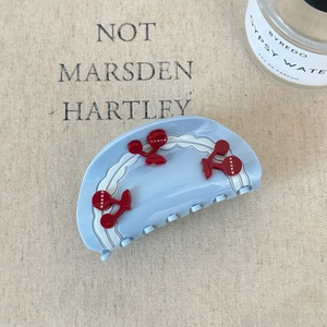 Detail of light blue acetate hair claw clip with red cherry patterns on beige linen