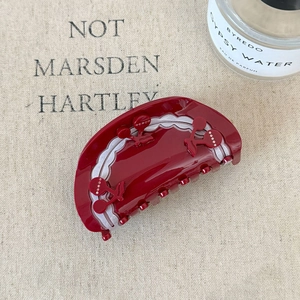 Detail of red cherry acetate hair claw clip with rhinestones on beige fabric backdrop