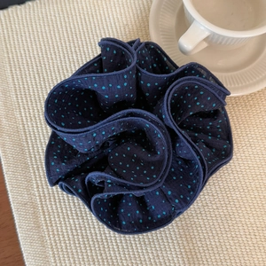 Navy blue polka dot hair scrunchie with layered ruffles on a cozy textured background