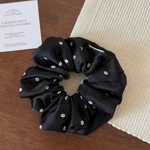 Dettaglio di un elastico in raso nero con stampa floreale bianca su sfondo rustico