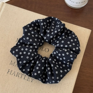 Close-up of black scrunchie with white floral pattern on a beige textured background