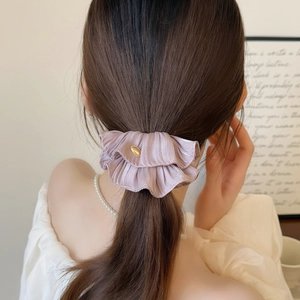 Detail of light purple pleated silk scrunchie with gold label on model ponytail