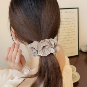 Champagne silk scrunchie with layered pleats and a gold metal accent on elegant hair
