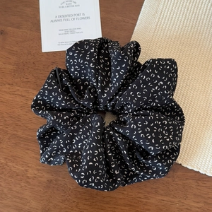 Detail view of the elegant black floral scrunchie on a rustic wooden tabletop