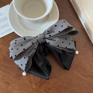 Detailed view of gray polka dot bow hair clip with pearl dangles on a wooden table