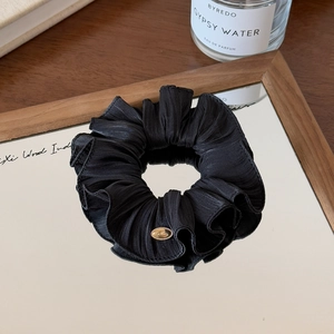 Detailed view of a black pleated silk scrunchie with a gold metal tag on a mirror