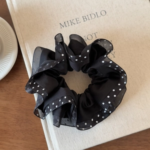Detail view of black polka dot mesh scrunchie with pleated edges on a book prop