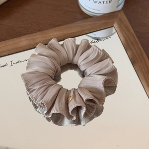 Detail of light brown silk scrunchie with golden metal logo on a wooden mirror