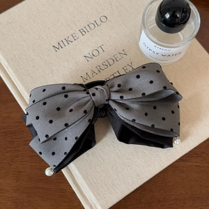 Detailed view of gray polka dot bow hair clip with pearls on a vintage book