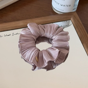 Detail of a dusty pink silk scrunchie with a gold logo tag on a mirrored surface