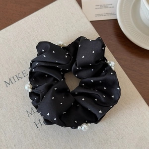 Vue détaillée d'un chouchou en satin noir à pois avec des accents de perles blanches élégantes