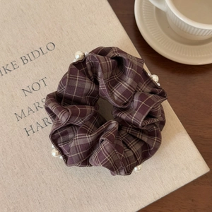 Detailed view of a brown plaid hair scrunchie with white pearl accents on an aesthetic book
