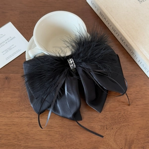 Detailed close-up of a black satin bow hair clip with feathers and rhinestones on wood