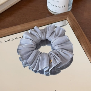 Detailed macro shot of lavender pleated scrunchie with a gold metal tag on a mirror