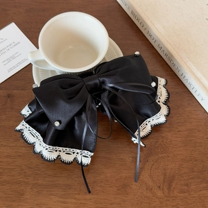 Detail of a large black satin bow hair clip with delicate white lace edges and rhinestones