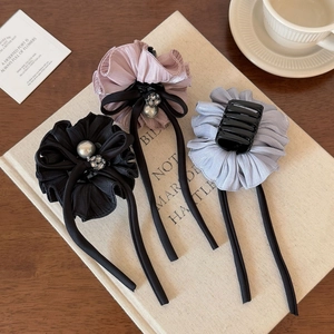 Detailed view of ruffle hair claws with ribbons and pearls in pink, black, and blue