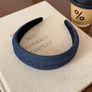 Detailed texture of dark blue denim fabric headband resting on a cream-colored cloth book