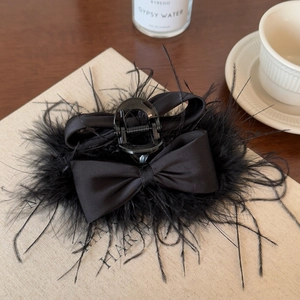 Elegant black feather hair claw clip with satin bow on a vintage book background