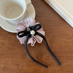 Detail of elegant hair clip with pleated fabric flower, pearls and long black ribbons