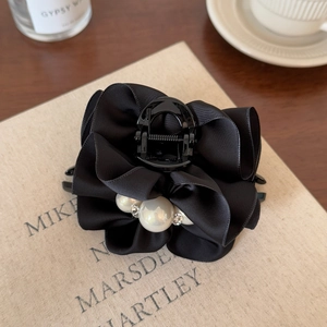 Pince à cheveux élégante en satin noir avec perles et strass posée sur un livre