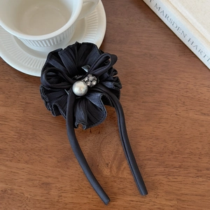 Detail of black ruffled fabric hair bow with a large pearl center and trailing ribbons
