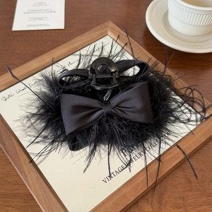 Detail of elegant black feather and satin bow hair claw clip on a mirror tray
