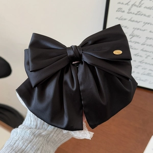 Gros plan d'une pince à cheveux à gros nœud en satin noir avec étiquette dorée