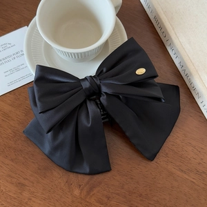 Détail d'une grande pince à cheveux avec nœud en satin noir et logo doré sur bois sombre