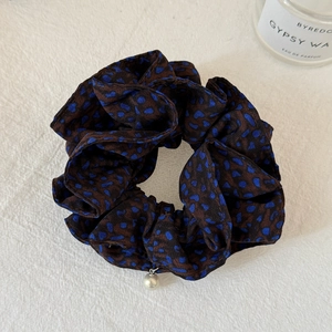 Detail view of brown polka dot scrunchie with a pearl charm on white fabric