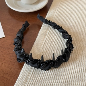 Close-up of black beaded headband with punk-style spikes on a warm wooden tabletop