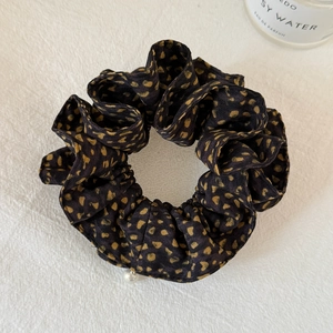 Close-up of black scrunchie with gold hearts and white pearl pendant on textile