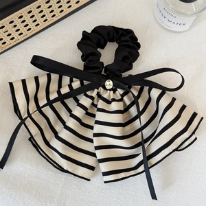 Detail of striped bow hair scrunchie featuring a golden pendant and black silk ribbons