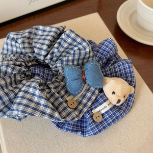 Vue détaillée du chouchou à carreaux bleus avec ours en peluche, nœud denim et bouton