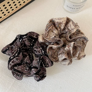 Detailed macro view of two vintage paisley print chiffon hair scrunchies on white fabric