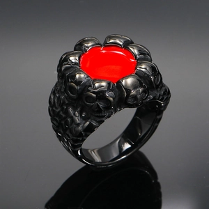 Detalle macro del anillo punk gótico con pequeños cráneos grabados y centro de esmalte rojo