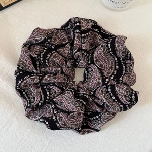 Close-up of black floral paisley scrunchie with elegant pleated fabric texture