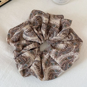 Close-up of beige Paisley print scrunchie with soft ruffled fabric texture on a white desk