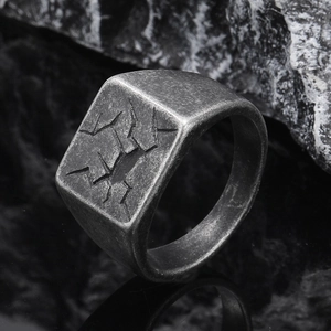 Makro-Detail eines quadratischen Titanstahlrings mit rissiger Textur auf dunklem Stein