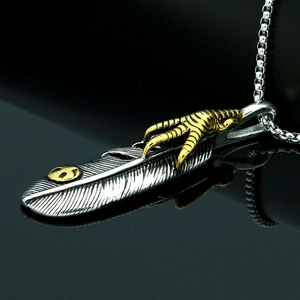 Macro detail of silver feather pendant with golden eagle claw on a black background